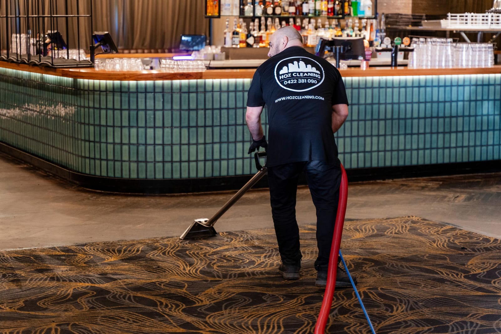 A HOZ CLEANING cleaner steam cleaning the carpet in front of a venue bar.